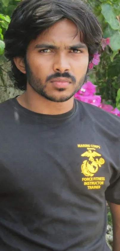 Man in black shirt standing amidst vibrant pink and green floral background.