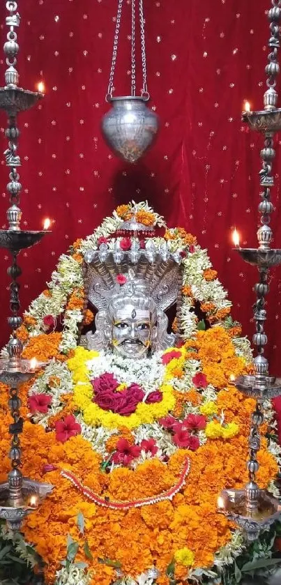 Floral deity sculpture with vibrant flowers and candles.