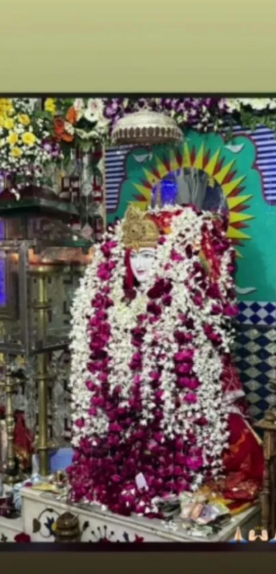 Deity adorned with red and white flower garlands against a vibrant backdrop.