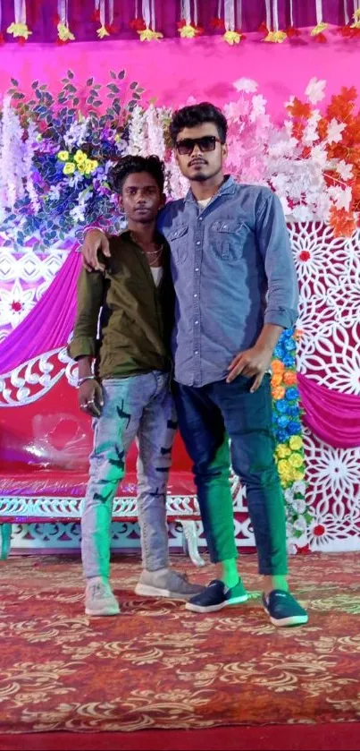 Two men posing at a colorful floral event with vibrant decorations.