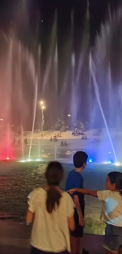 Colorful night fountain show with lights reflecting on water.