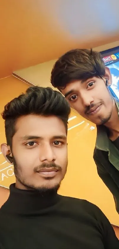 Two friends taking a selfie with an orange background on a mobile phone wallpaper.