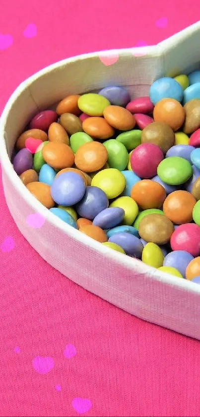 Heart-shaped box filled with colorful candies on a pink background.