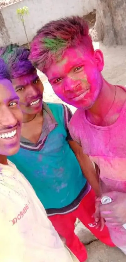 Three friends smiling with colorful Holi powders on their faces.