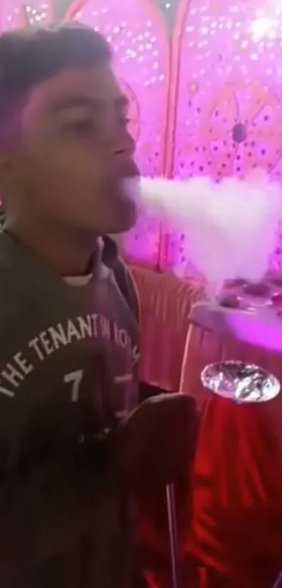 Man exhaling hookah smoke against a pink backdrop.