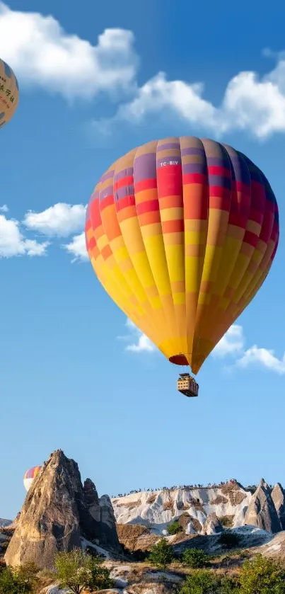 Colorful hot air balloons floating over rocky landscape and blue sky.