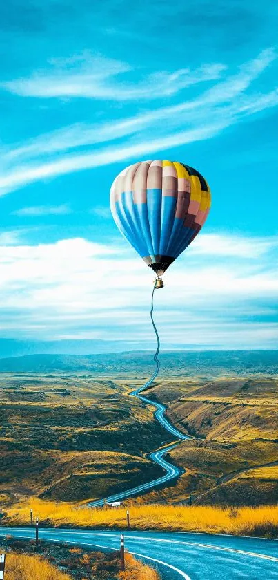 Vibrant hot air balloon above scenic road in sky blue landscape.