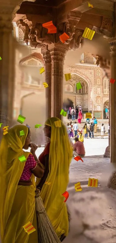 Two women in traditional attire amidst colorful confetti in an Indian palace.