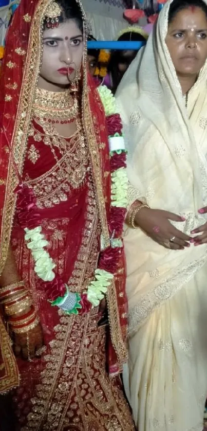 Indian bride in red sari with woman in white dress at wedding.