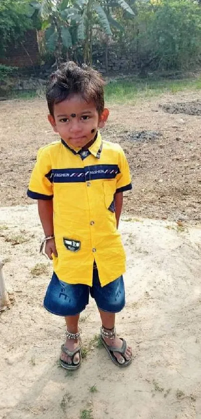 Young boy in a yellow shirt outdoors with a joyful expression.