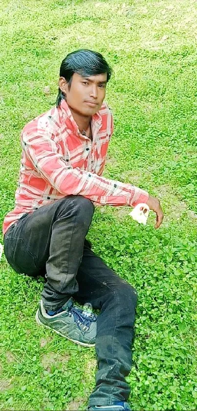 Man in red shirt sitting on green grass.