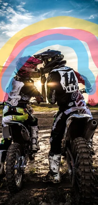 Two motocross riders in front of vivid rainbow and sunset backdrop.