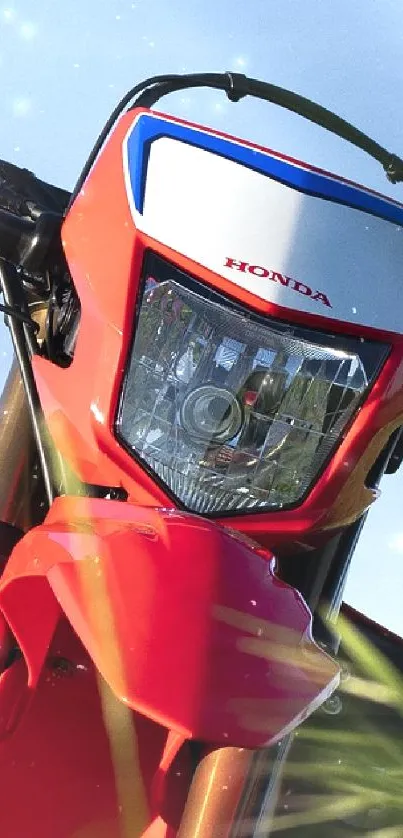 Red motorcycle in a green field under blue sky.