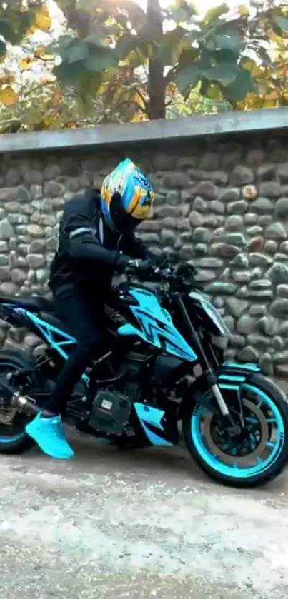 Motorcycle rider with turquoise bike near stone wall.