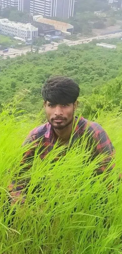 Person sitting in lush green grass with city in the background.