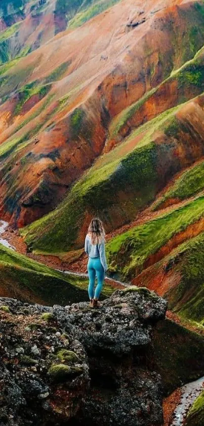 Person standing on a vibrant colorful mountain with lush green and orange hues.