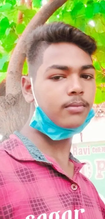 Young man posing in front of vibrant green leaves with a mask.