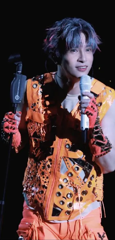 Singer in vibrant orange outfit on stage with microphone.