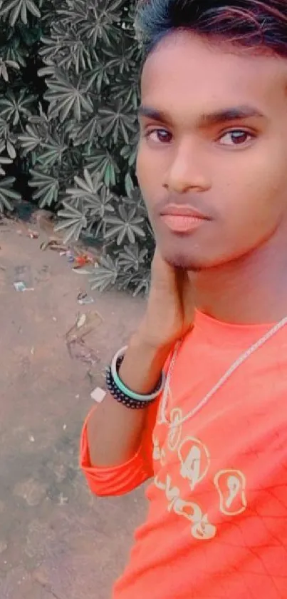 Young man in vibrant orange shirt with natural leafy background.