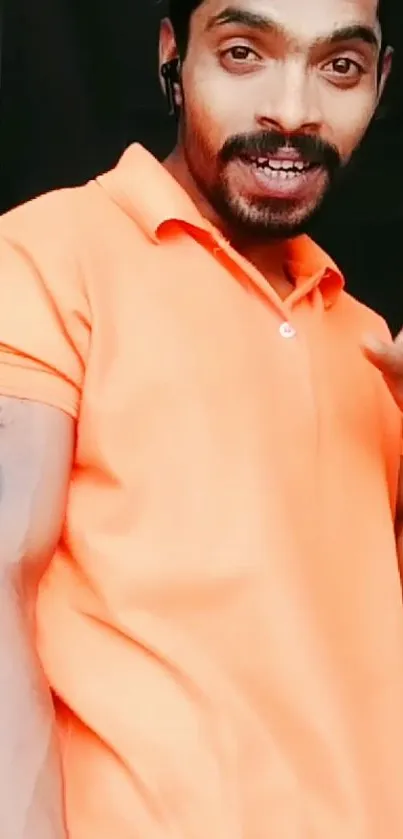 Confident man in orange shirt posing stylishly for mobile wallpaper.