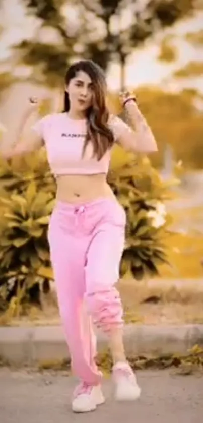 Woman dancing in pink outfit outdoors against a warm yellow background.