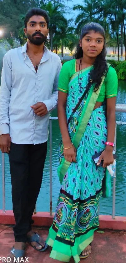 Couple on bridge with lake and greenery in the background.