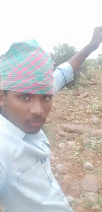 Young man posing outdoors with greenery and rock landscape.