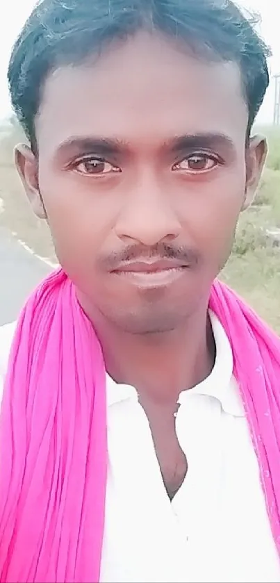 Person standing outdoors with a pink scarf around the neck, on a nature backdrop.