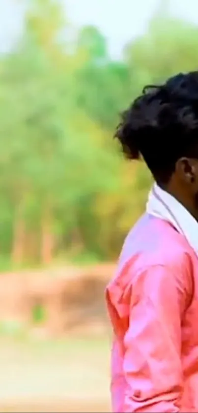 Man in pink shirt outdoors with lush green backdrop.