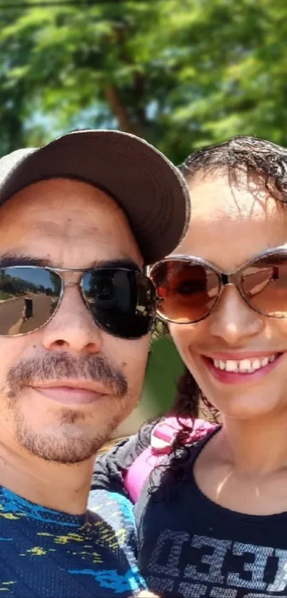 Smiling couple outdoors in sunglasses with a green backdrop.