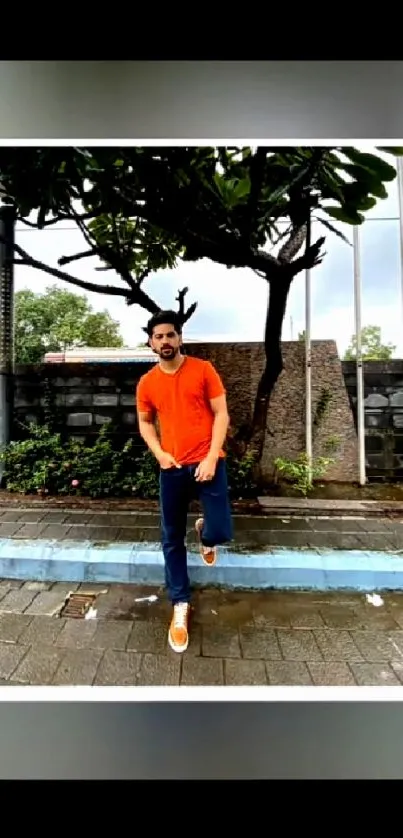 Man in orange shirt outdoors with urban backdrop.