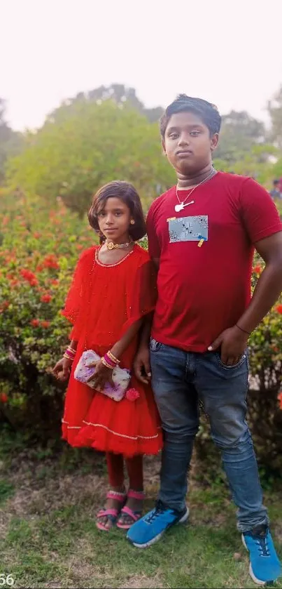 Children standing in a park wearing red outfits with green foliage background.