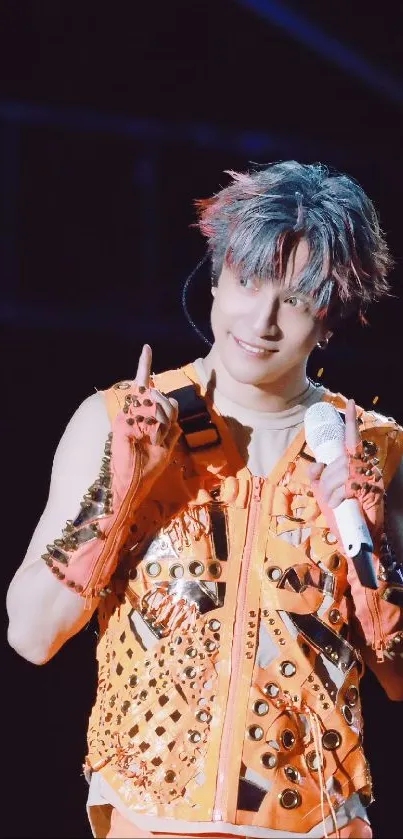 Performer in vibrant orange outfit singing energetically on stage.