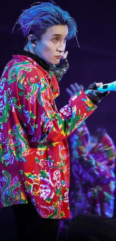 Performer in vibrant floral shirt on stage with blue lighting.