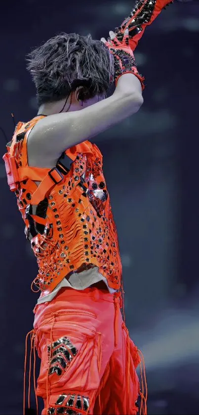 Performer in vibrant orange outfit on stage.