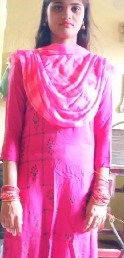 Woman in vibrant pink traditional dress standing indoors.