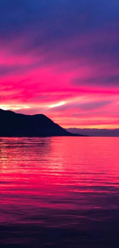 Vibrant pink sunset over calm ocean waters with silhouetted mountains.