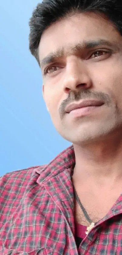 Man in checkered shirt against a soft blue background.