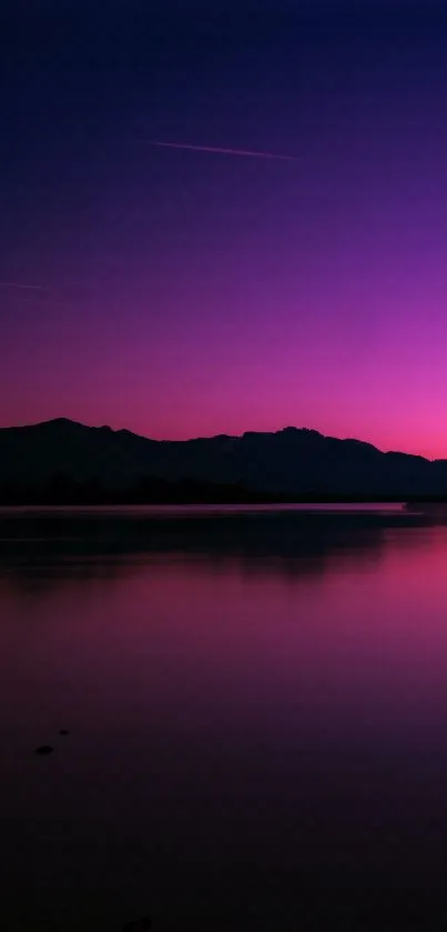 Vibrant purple sunset over tranquil waters with a scenic mountain silhouette.