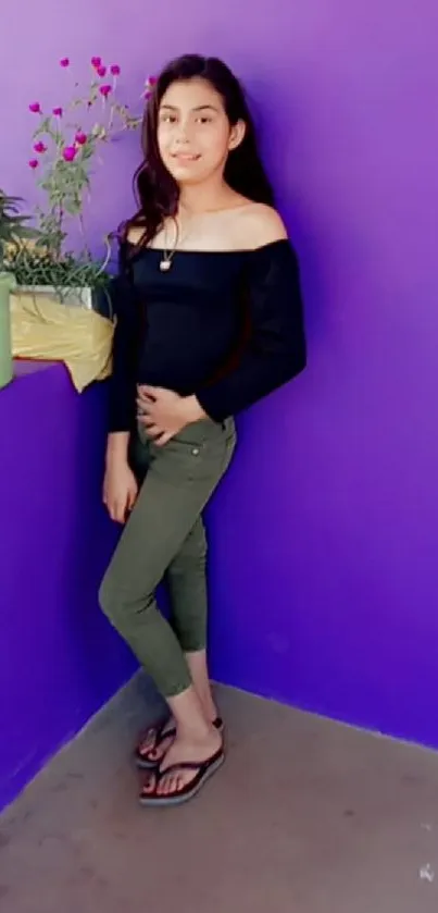 Girl posing against a vibrant purple wall with flowering plants.