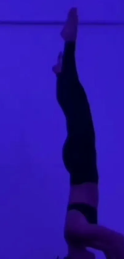 Silhouette of a person doing a headstand against a deep purple background.