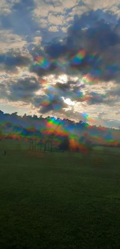 Rainbow effect through clouds at sunrise over a green field.