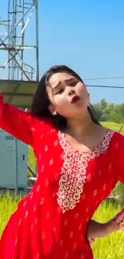 Person in red dress outdoors with green field and blue sky.