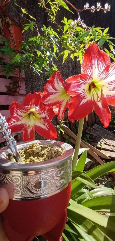 Hand holds ornate cup next to red flowers.
