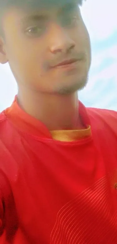 Person wearing a red shirt with a soft sky background.