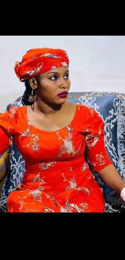 Woman in vibrant red traditional dress seated on patterned sofa.