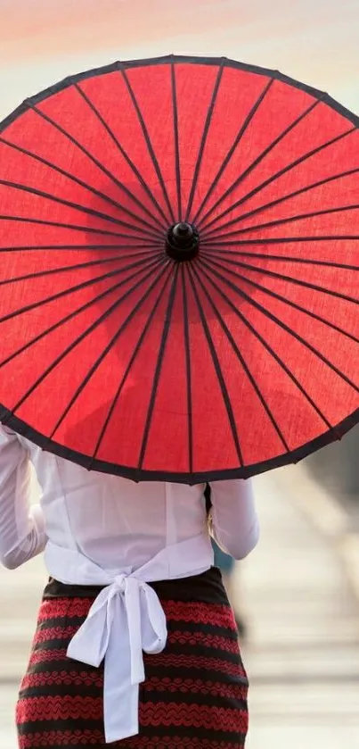 Image of a person with a vibrant red umbrella walking on a bridge.