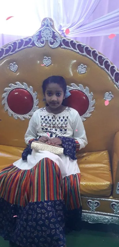 Child sitting on ornate golden throne in traditional attire.