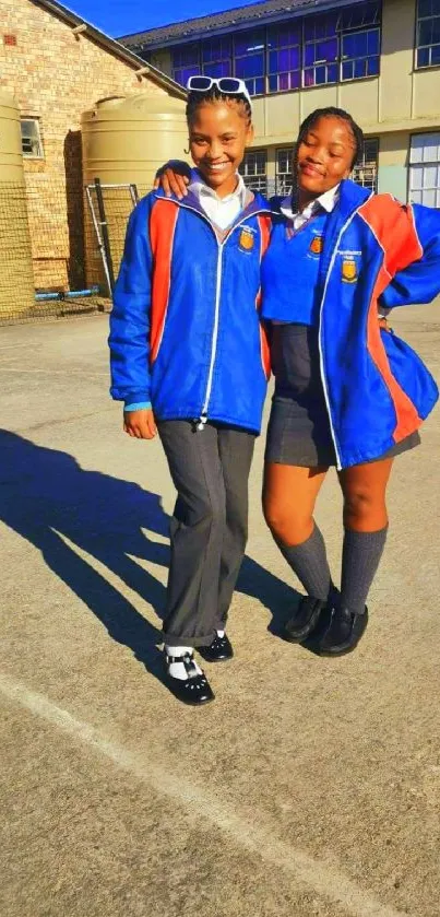 Two students in blue uniforms smiling in schoolyard.