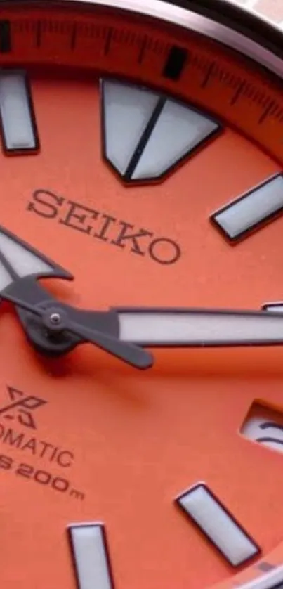 Close-up of an orange watch face with sleek metallic details on a mobile wallpaper.